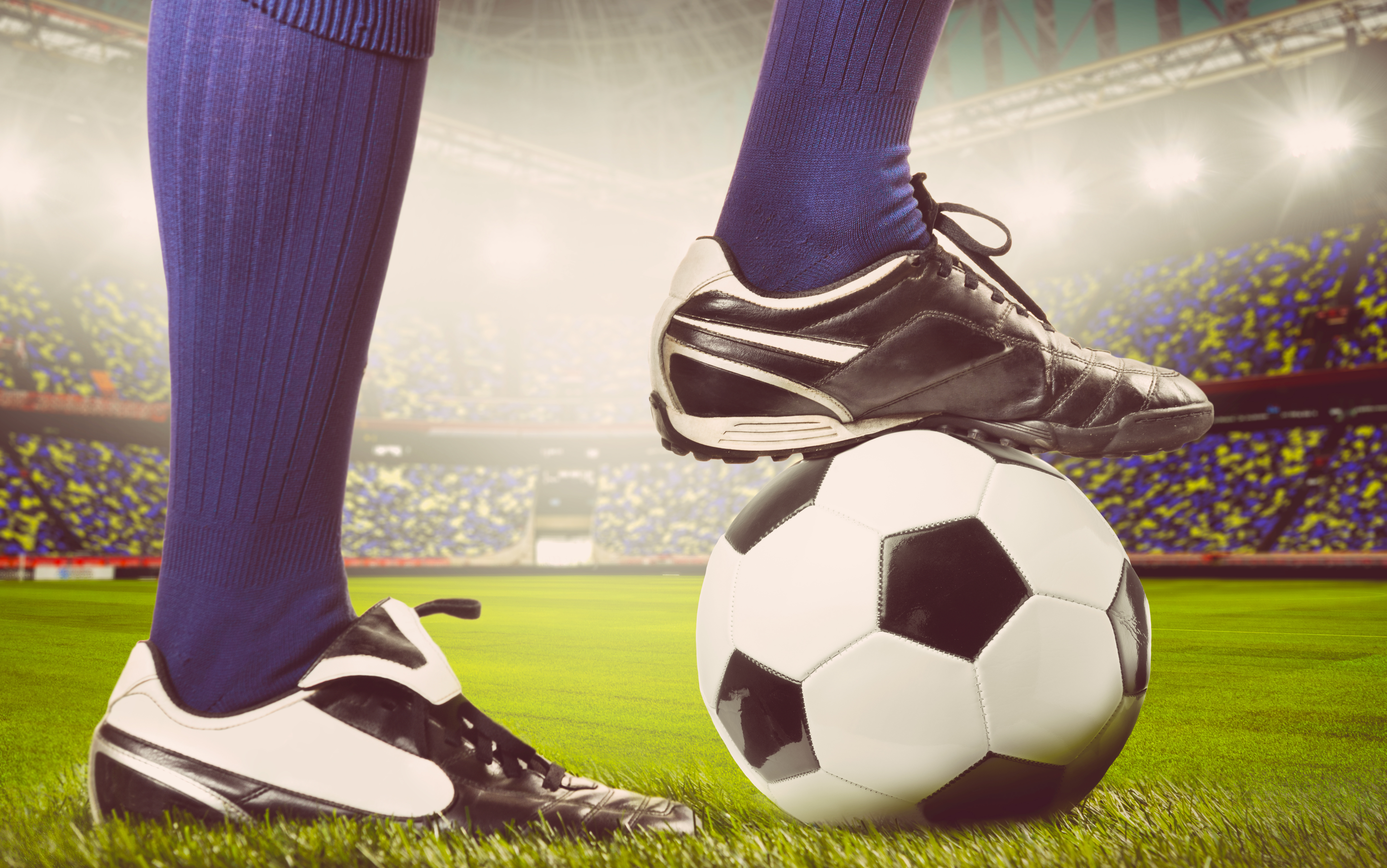 legs of a soccer or football player on ball on stadium, warm colors toned