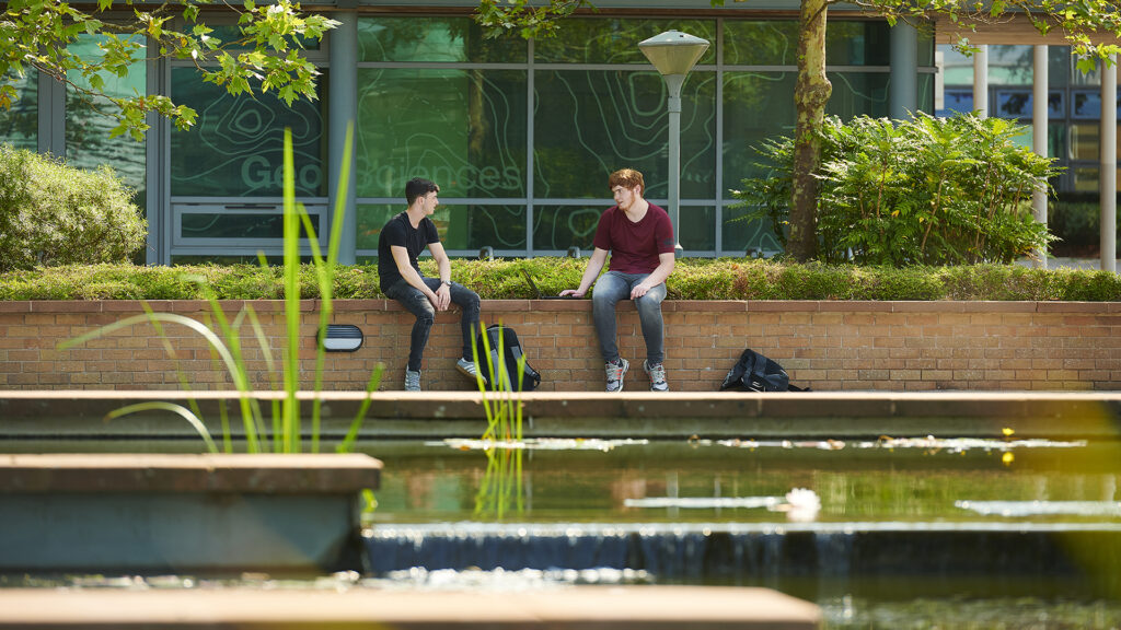2 students chat outside the History, Geography and Social Sciences building.