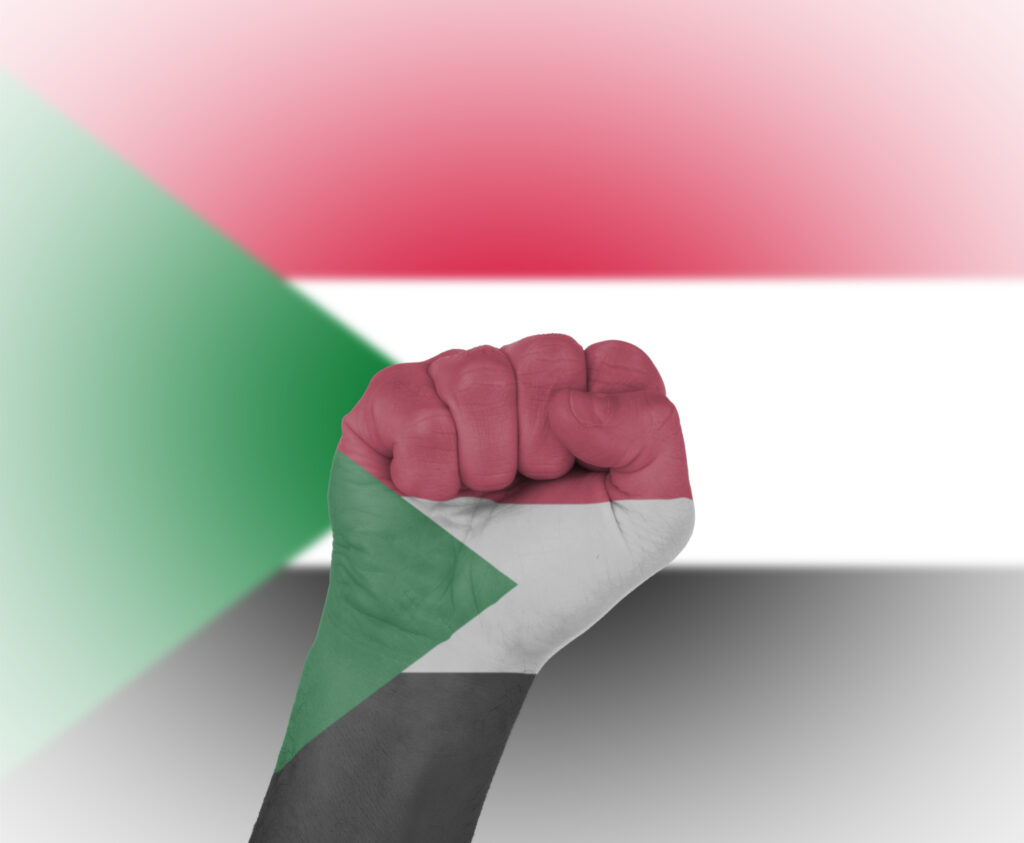 A fist painted the colours of the flag of Sudan and flag in the background