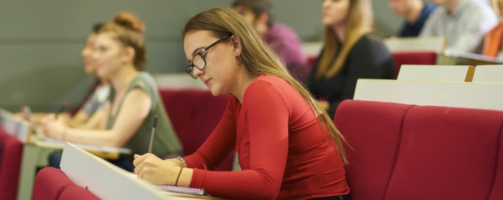 Students in lecture theatre one is taking notes whilst others are listening to the tutor.