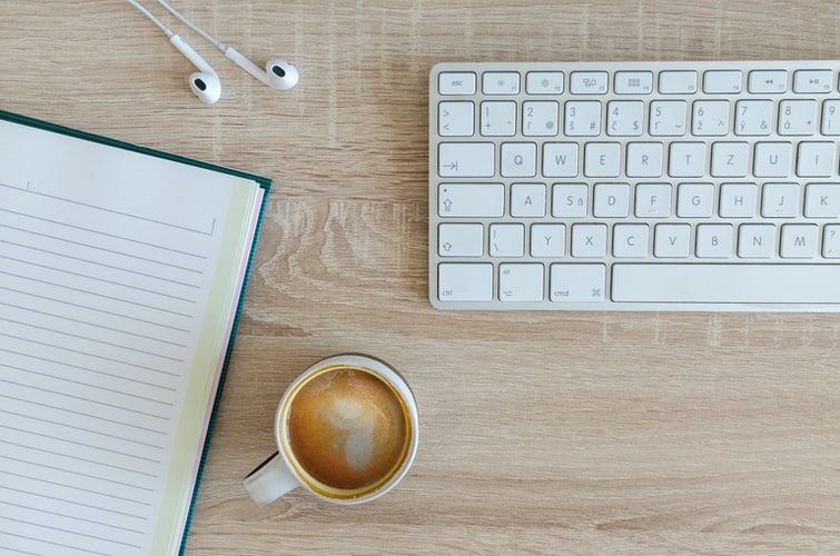 Photograph of office work desk including a keyboard, writing notebook and cup of coffee.