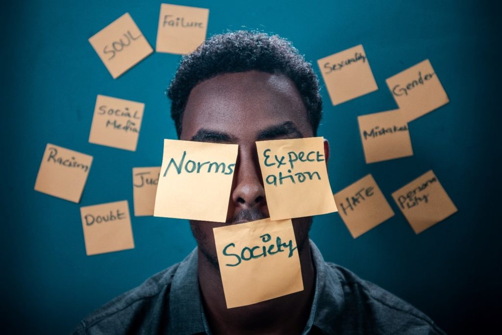 Photograph of person surround by sticky notes. Notes contain words including: norms, expectation and society. 
