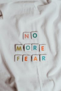 Image of colourful letters printed on small square tiles, they are arranged to read 'NO MORE FEAR' and sit on a white cloth background.