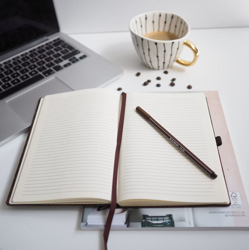 notebooks with a pen on top, next to a laptop with a cup of tea next to them