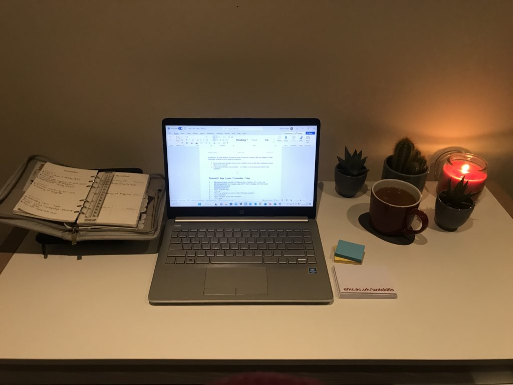 a laptop on a desk with a candle, diary, and UniSkills sticky notes