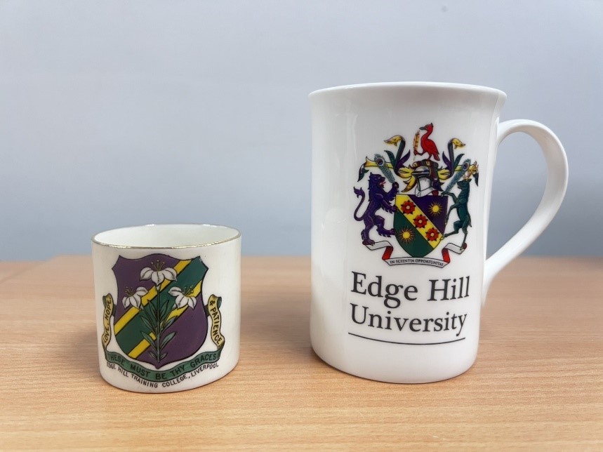 Two cups sitting side by side on a table top. Both cups have Edge Hill crests on them. However, the cup on the left is less than half the size of the cup on the right. 