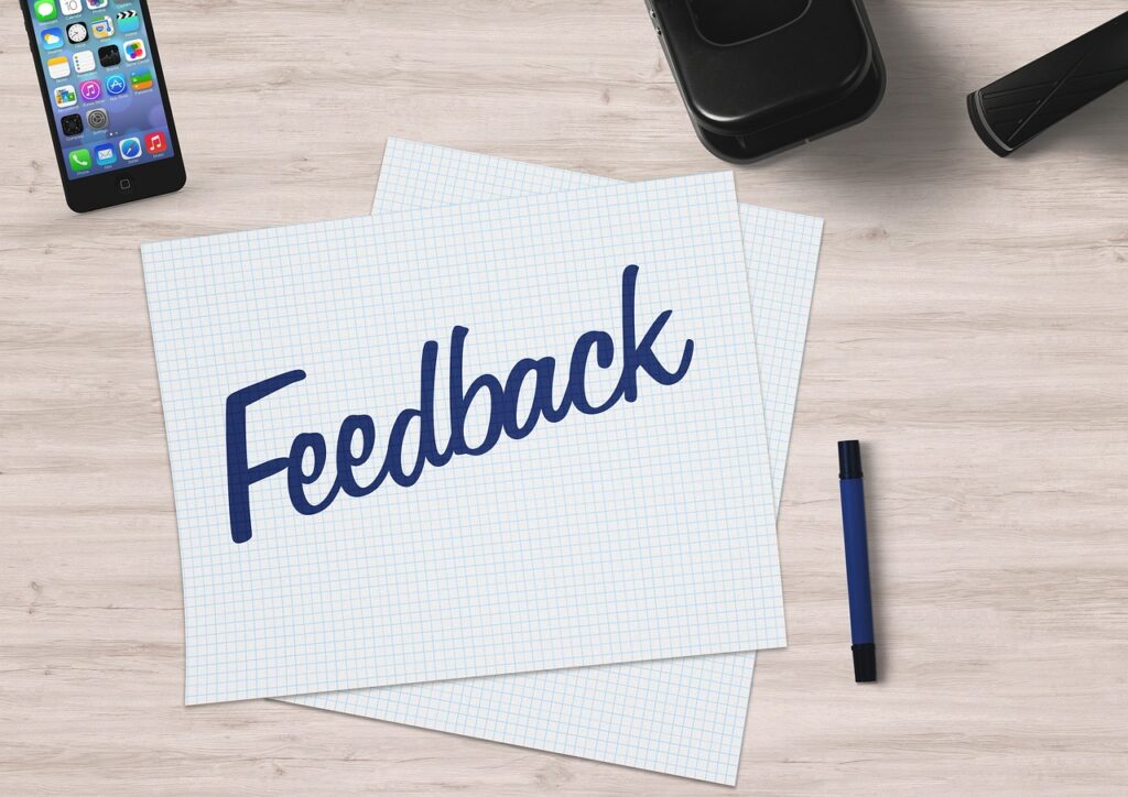 Desk with a mobile phone and pen on it. On the middle of the desk are two sheets of graph paper and one of them has the word 'feedback' written on it in blue pen.