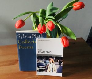 Red tulips overhang from a vase, onto two Sylvia Plath books of poetry, 'Collected Poems' and 'Ariel'.
