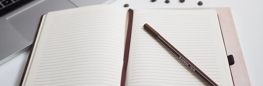 notebooks with a pen on top, next to a laptop with a cup of tea next to them