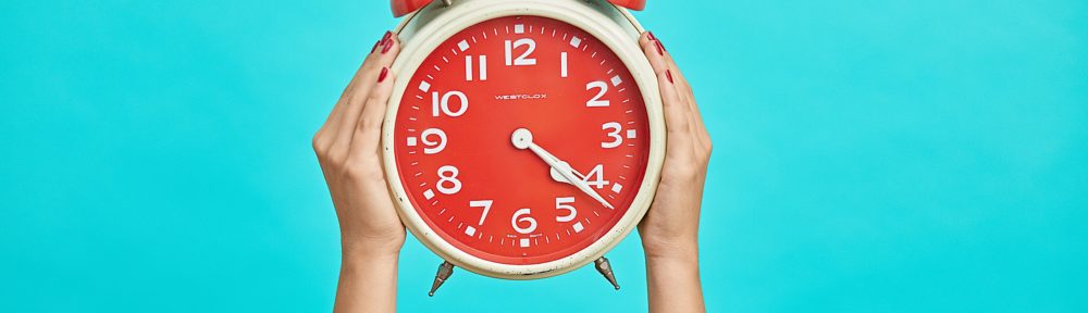 Red alarm clock being held in the air, against a blue background