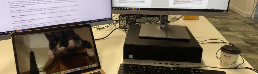 a laptop connected to a screen with an image of a cat and a note book