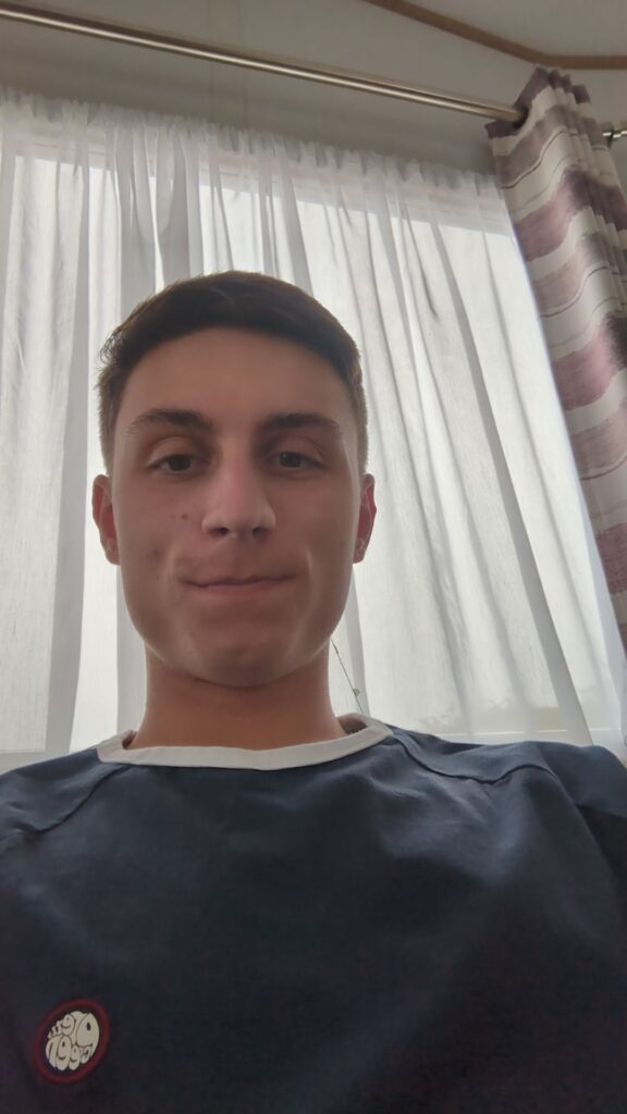 Student Advisor Lewis Underwood. Lewis has short brown hair and is wearing a blue t shirt.