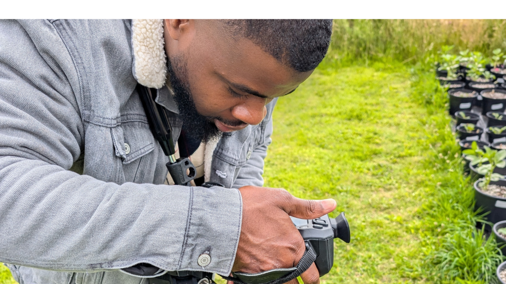A boy leaning over, looking at a camera. He is taking images of plants. 